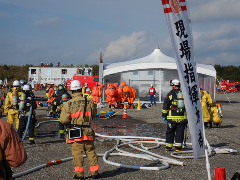 化学剤がまかれた建物から防護服を着た隊員が要救助者を救出している写真
